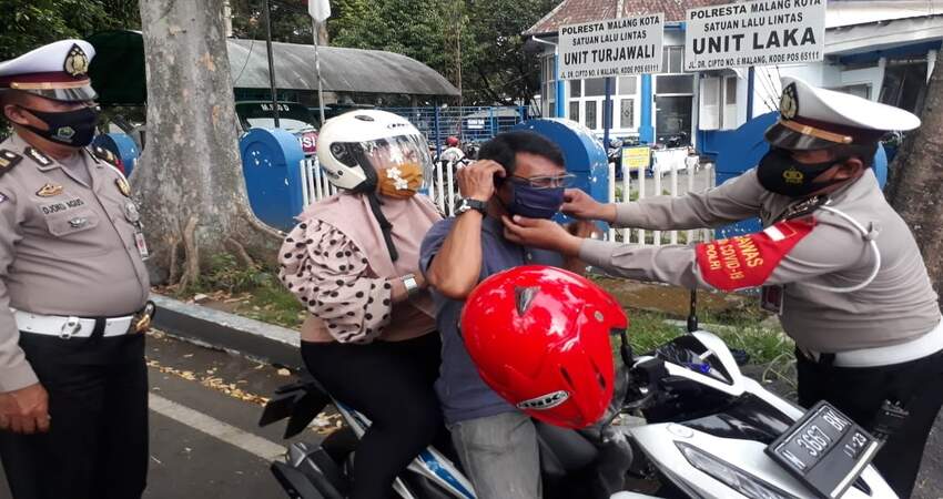 Kasubnit I Laka Lantas Polresta Malang Kota Ipda Deddy saat memakaikan masker kepada pengguna kendaraan . (gie)